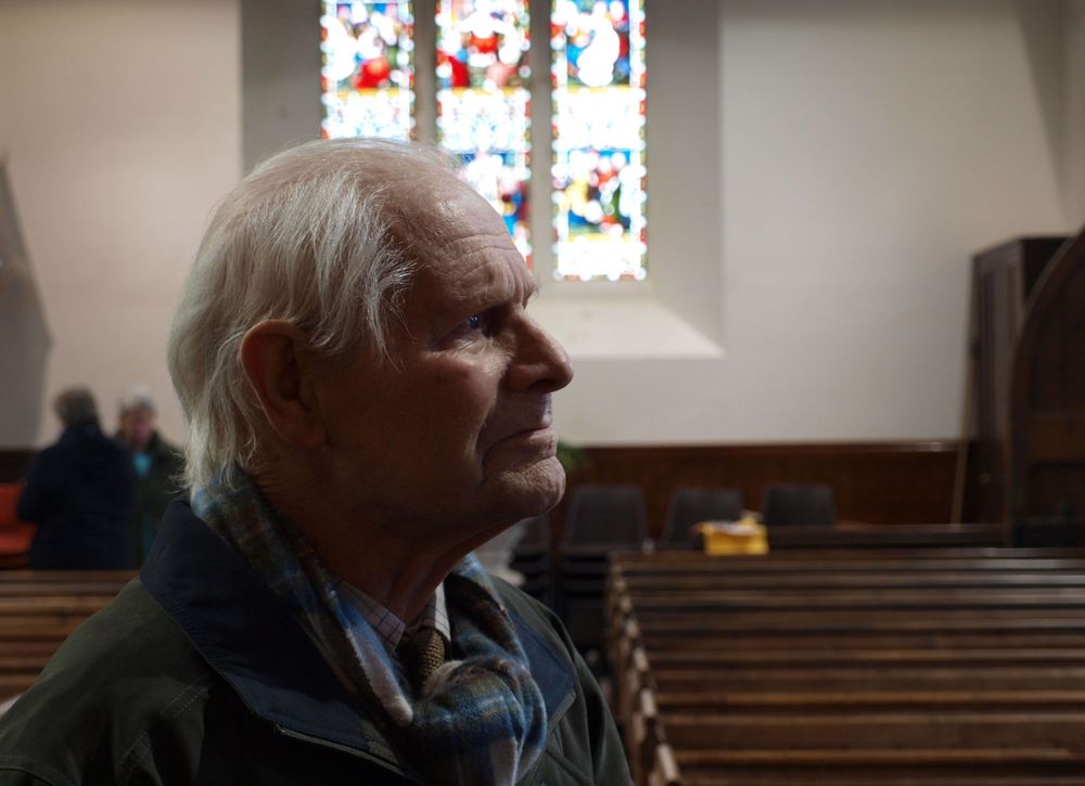 Portrait of Lawrence Stanley Lee (1909-2011) in a church interior looking at his stained glass window.