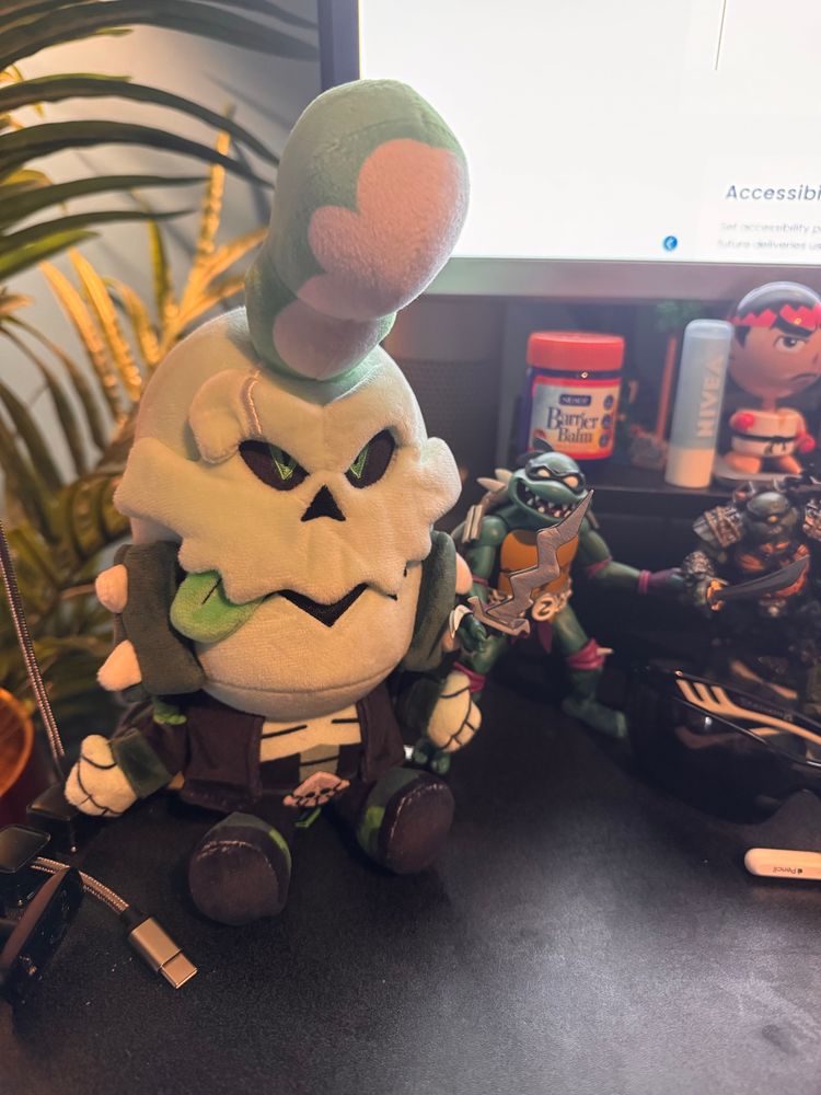 A plush figure of a character from Monkey Wrench named Jae Bone, who is a skeleton with a leather jacket, a pompadour and its green tongue stuck out of one corner of its face. Next to it are two figures of the Ninja Turtles character, Slash.