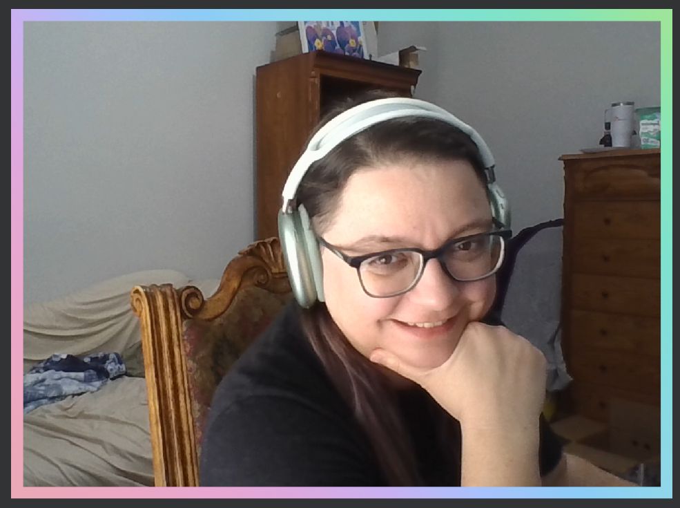 Linda grins goofily into the camera, resting her chin in the crook of her hand between her thumb and the rest of her fingers.