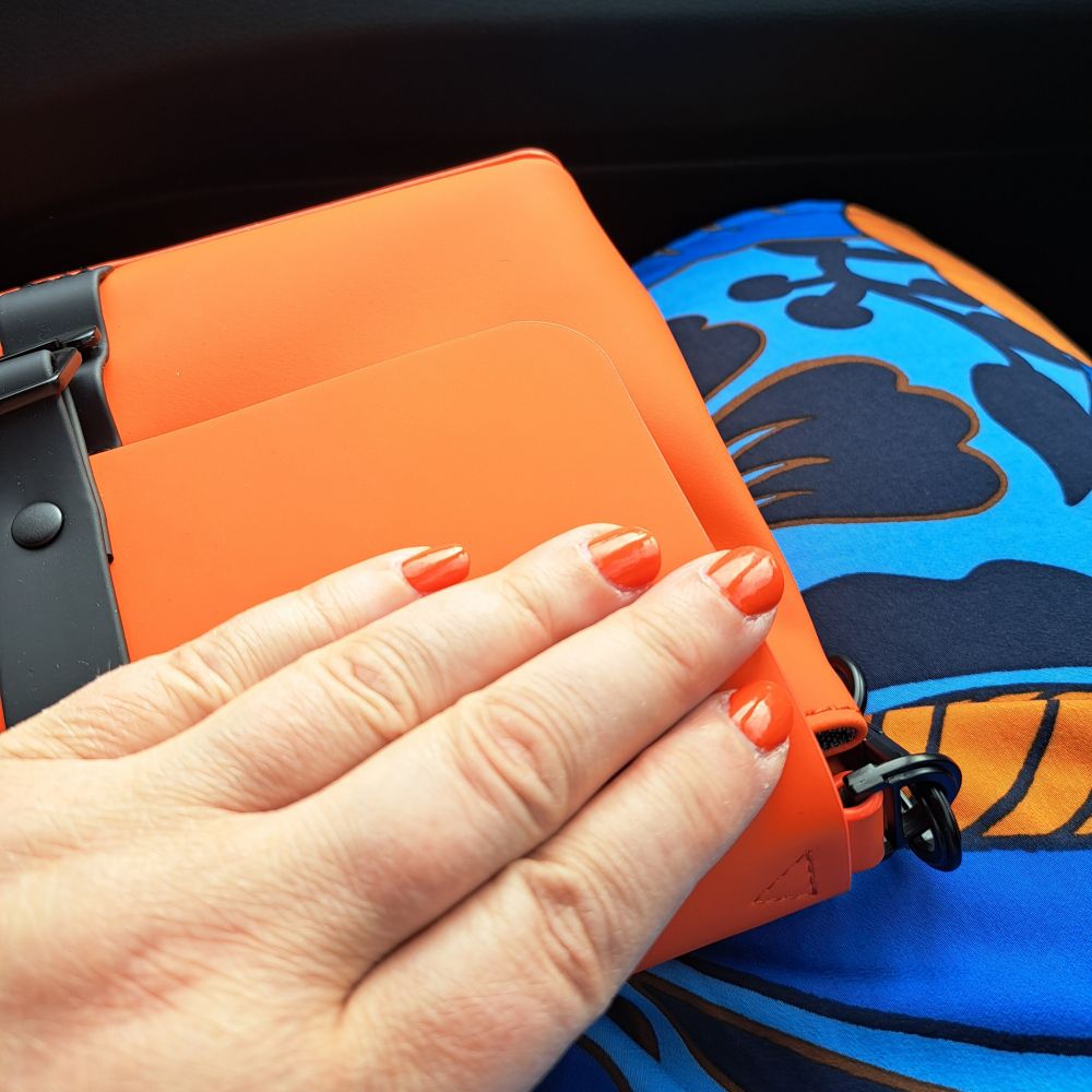 Hand mit orangem Nagellack, orange Handtasche und ein blau orange gemustertes Kleid