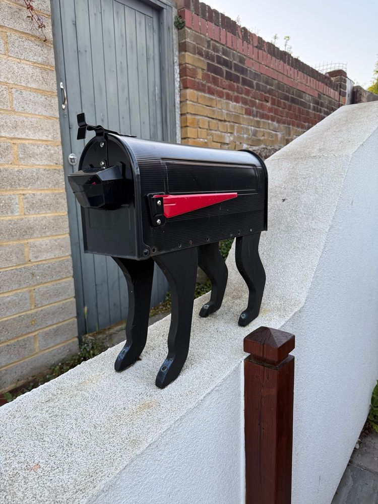 A black postbox (mailbox) on a wall with cat legs and a red handle