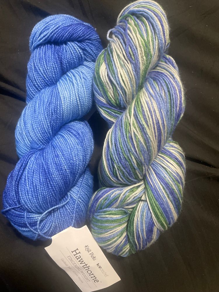 A blue tonal skein and a blue, green, and white skeins of yarn 