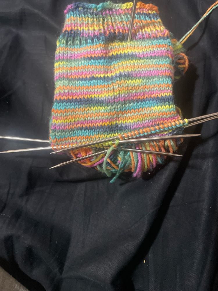 Fluorescent rainbow striped sock leg on four knitting needles.