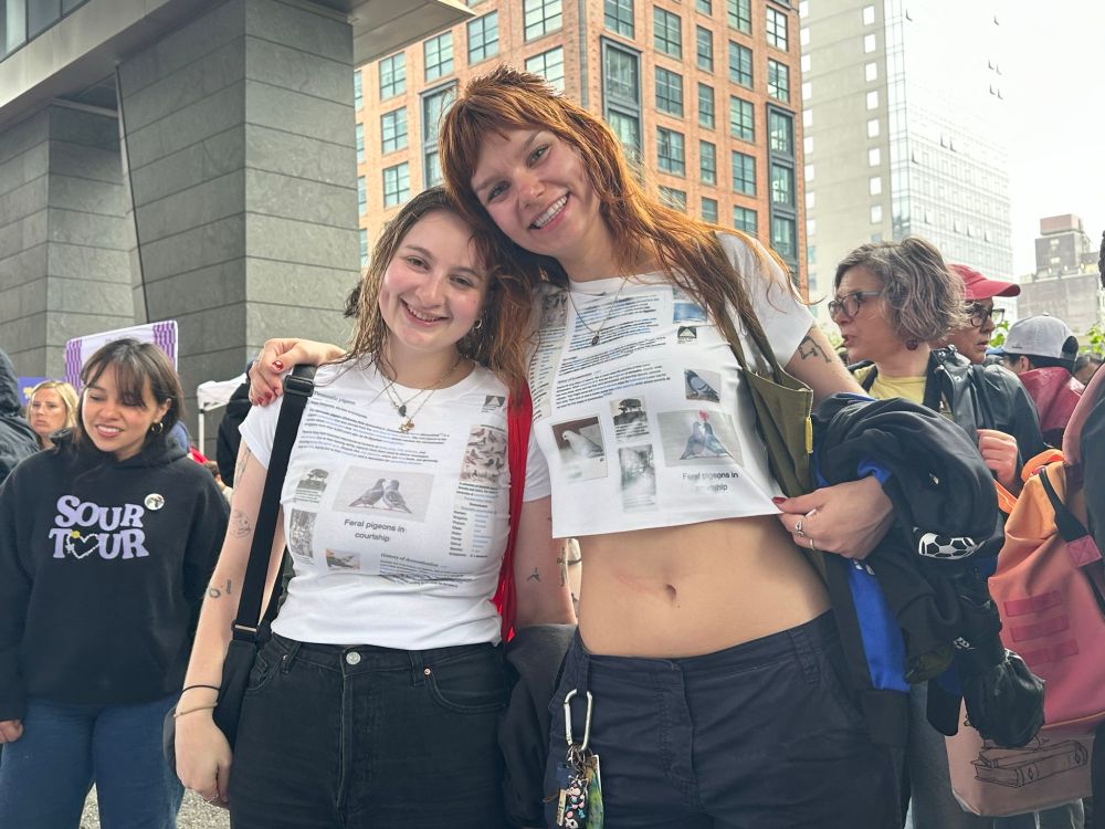 Two women wearing tshirts that are printed with the wikipedia article on pigeons.