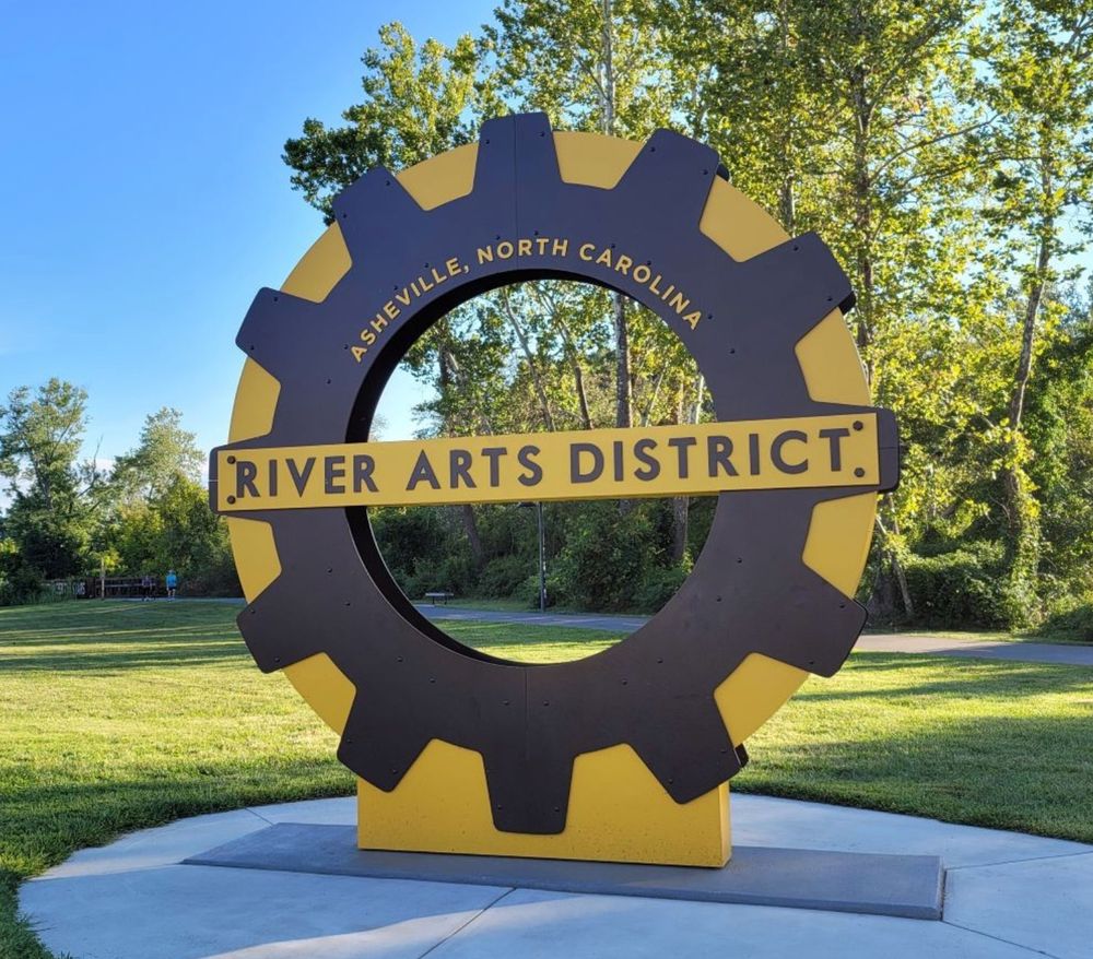 An image of a yellow and brown gear-shaped sculpture labeled "Asheville, North Carolina River Arts District" with a link riverartsdistrict.com.