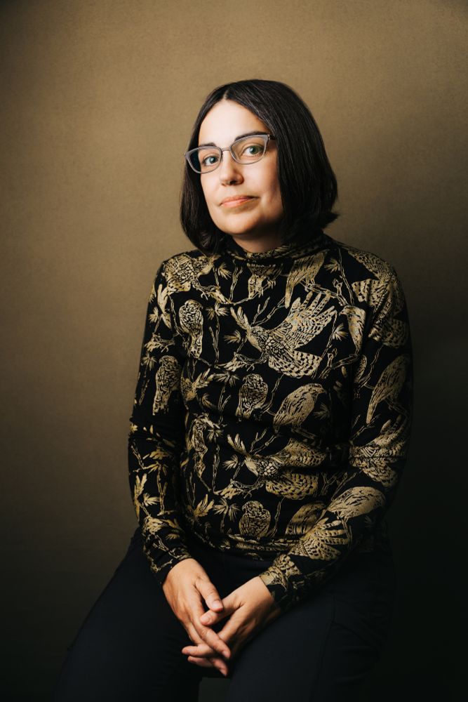 A woman with short brown hair and a black collared shirt with gold birds of prey.