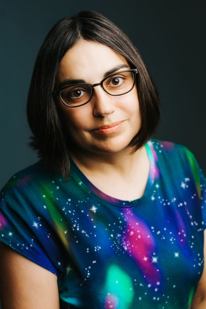 A woman with short brown hair, glasses, and a galaxy patterned shirt.