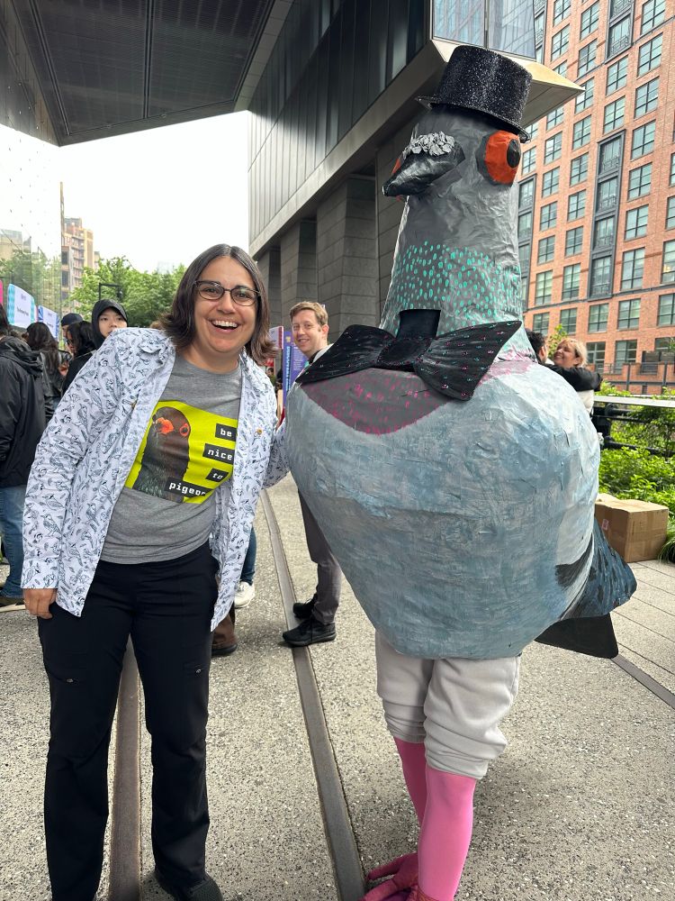 A woman wearing a pro pigeon shirt stands next to a person dressed like an enormous pigeon 