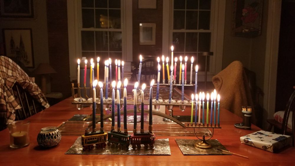 Five menorahs with eight lit candles each on a table in a darkened dining room