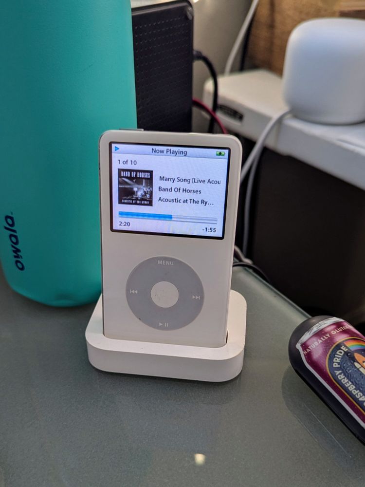 A white iPod classic in a docking cradle on a desk. 