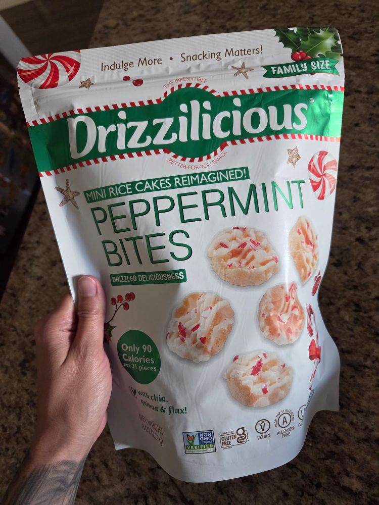 A bag of Drizzilicious, they are mini rice cakes and this particular bag is peppermint flavored. The bag is white, green, and a hint of red. There are pictures of mini rice cakes drizzled with white frosting and red peppermint pieces. Also pictures of various types of peppermint candies. There is an overall Christmas theme.