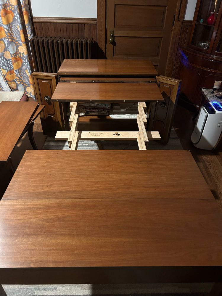 A wooden sideboard with a hidden four-leaf dining table extended. Two leafs are in place showing peg joinery and accordion frame underneath. 