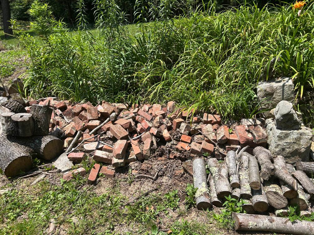 Daylight color photo of a messy pile of bricks bookended by stacked wood. 