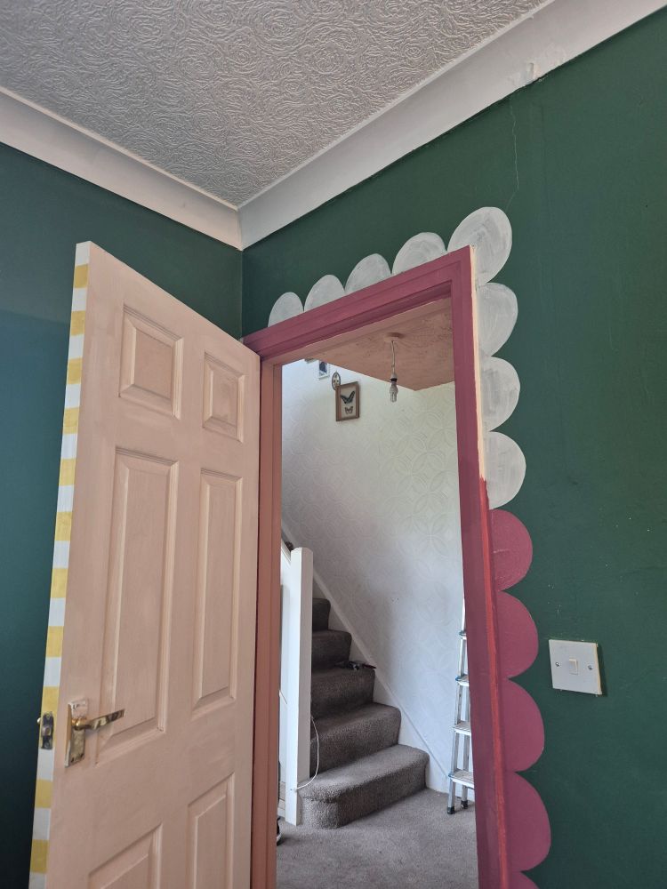 White door with yellow and white stripey edge, green walls and half painted dusky paint scallop edging around the door. Through the door you can see really ugly brown carpet..