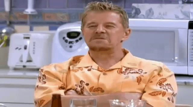 a man wearing a hawaiian shirt is sitting at a table with his eyes closed