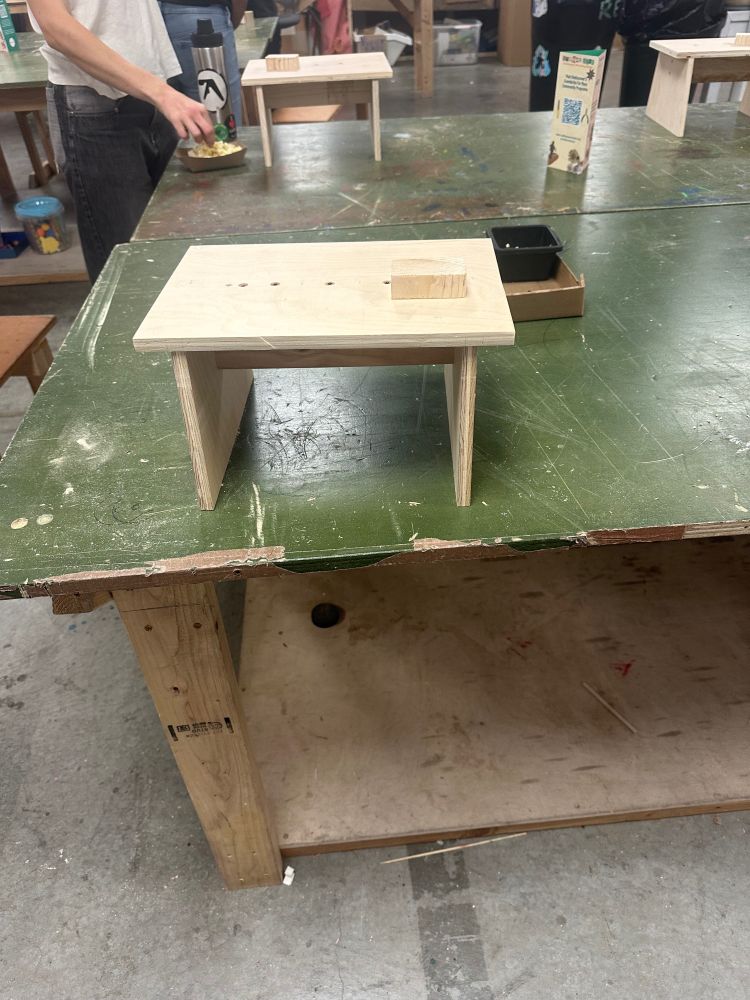 picture of an unstained wooden stool on a green table 