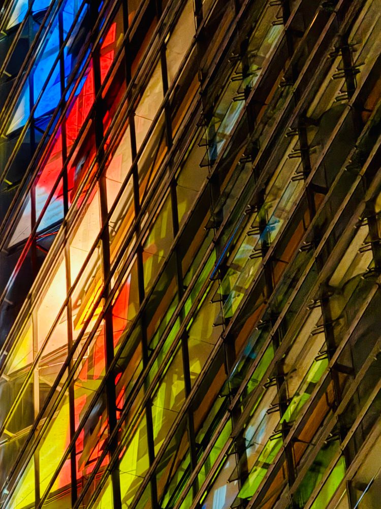 Ausschnitt einer bunt illuminierten Hochhausfassade. Das am Ende spitz zulaufende Haus wurde in der Dunkelheit aus der Froschperspektive fotografiert.