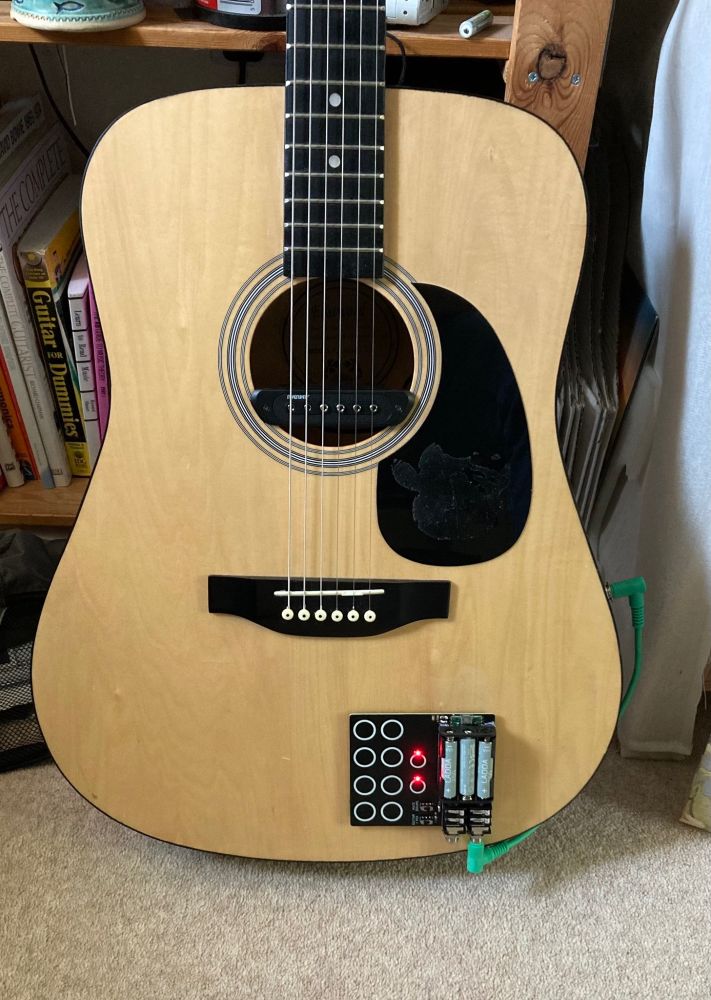 An steel strung acoustic guitar fitted out with a soundhole magnetic pickup. Mounted on the guitar using Velcro is a home made drum machine to generate percussive sounds for use with a looper pedal.