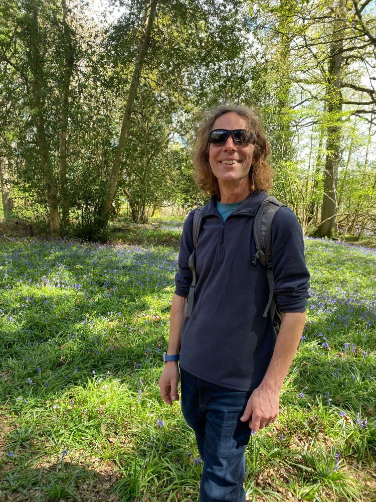 It’s me, with a backpack on, standing in a natural wooded area full of bluebells. 