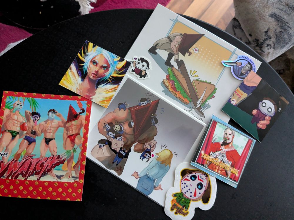 Picture of small prints and stickers showing slashers on the beach wearing swimwear. Two small stickers with Michael Meyers and a few small goodies and Jason Vorhees as an animal crossing character and two prints with pyramidhead in one he's cutting a sandwich with his sword and in the second he is handing little Michael Meyers to Laurie Strode