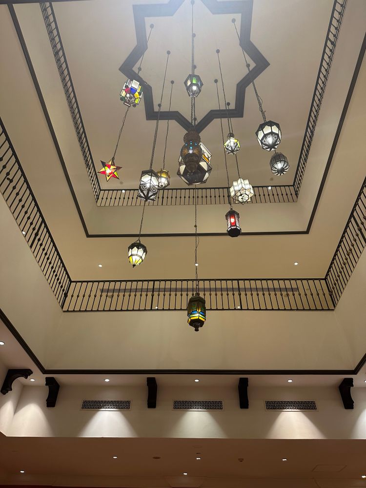 Multiple colorful stained-glass lamps hang from a chandelier frame in a three-story high ceiling. 