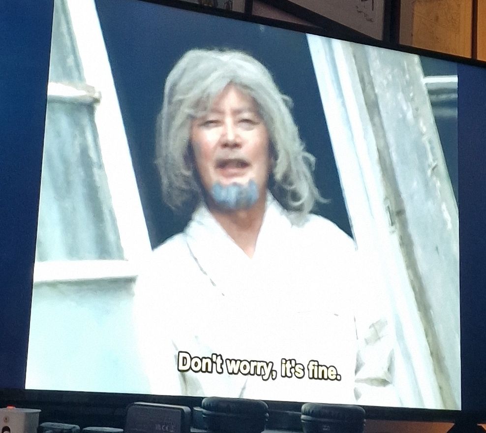 An old dishevelled man looks out a window.