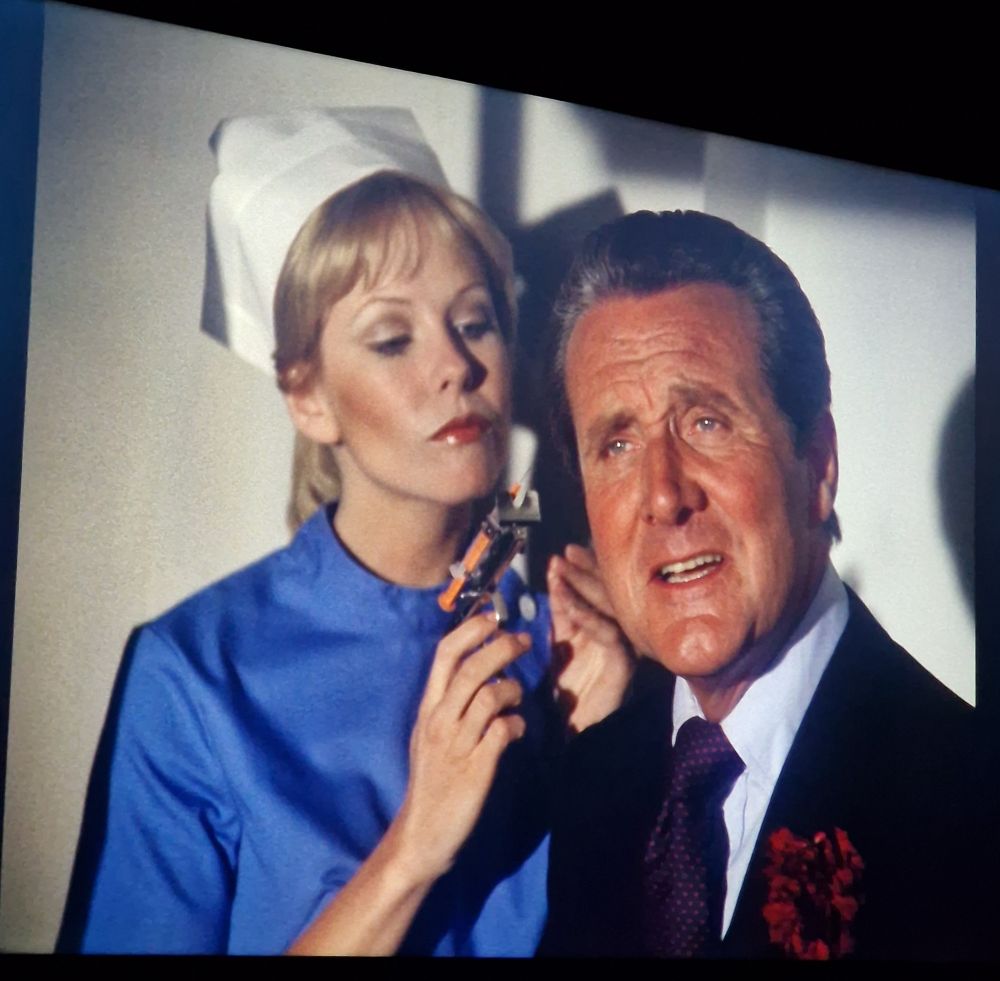 Pamela Stephenson (dressed as a nurse) looms behind Steed with a syringe.