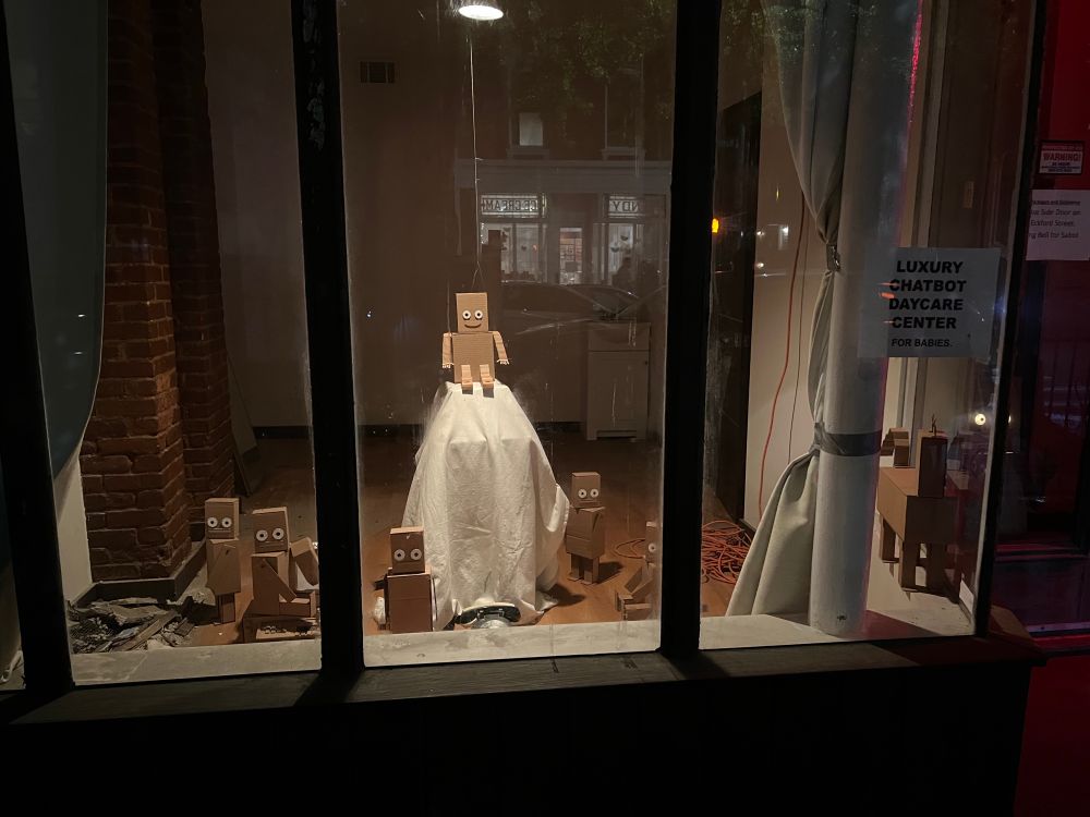 The same happy robot on the white table, zoomed out showing several other little robots on the ground all looking busy