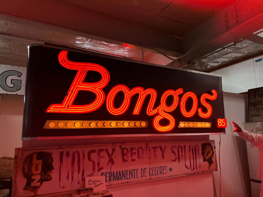 A red neon sign reading Bongos 85. It’s made up of three strips of 10mm tube forming a serif scrip word underlined with incandescent bulbs 