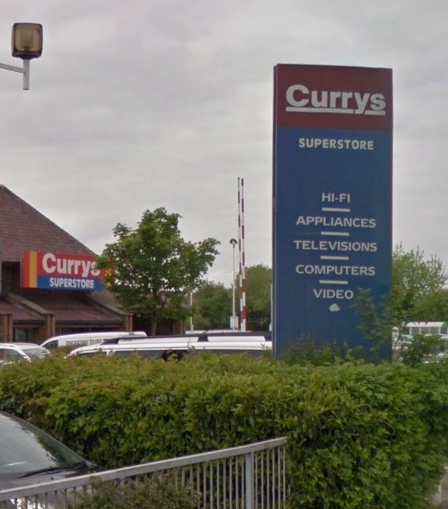 A Currys Superstore totem sign in a car park reading "Hi-fi, appliances, televisions, computers, video"