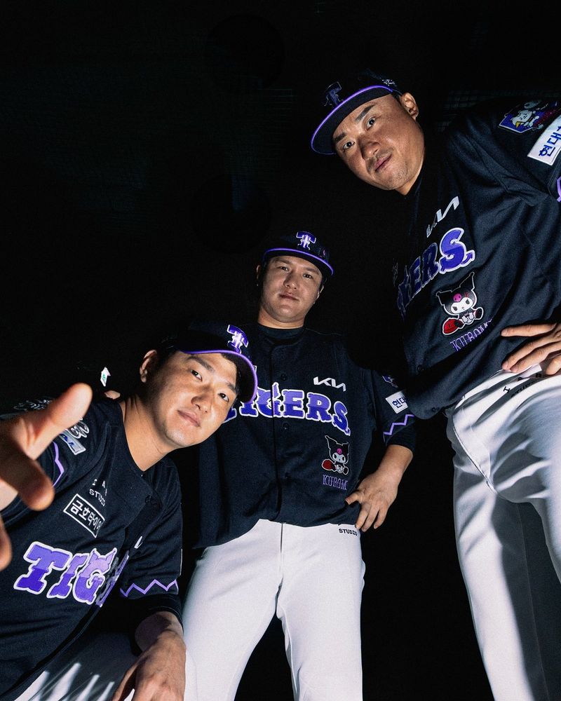 쿠로미 캐릭터가 그려진 검은색 기아 타이거즈 유니폼을 입은 건장한 남성 세 명을 아래에서 올려다본 모습.