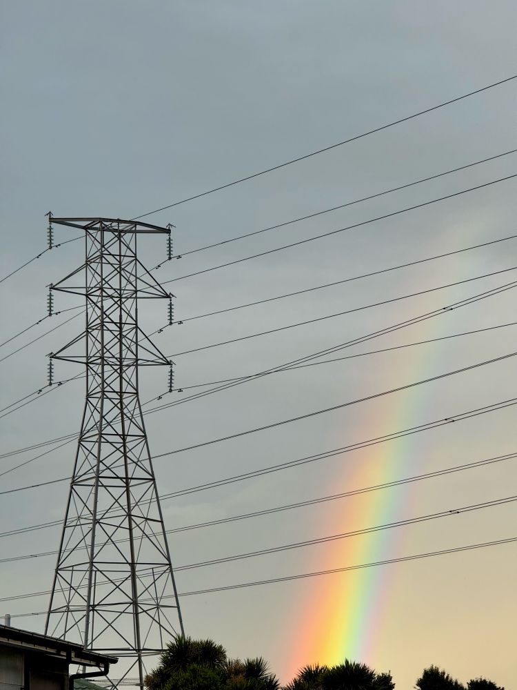 A large pylon and electrical cables towering above the camera, with a rainbow in the background