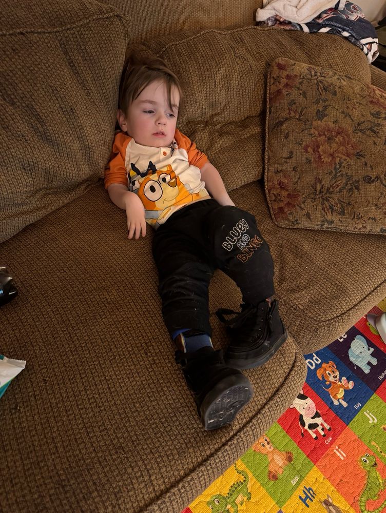 A toddler sitting exhaustedly on a old beat up brown couch 