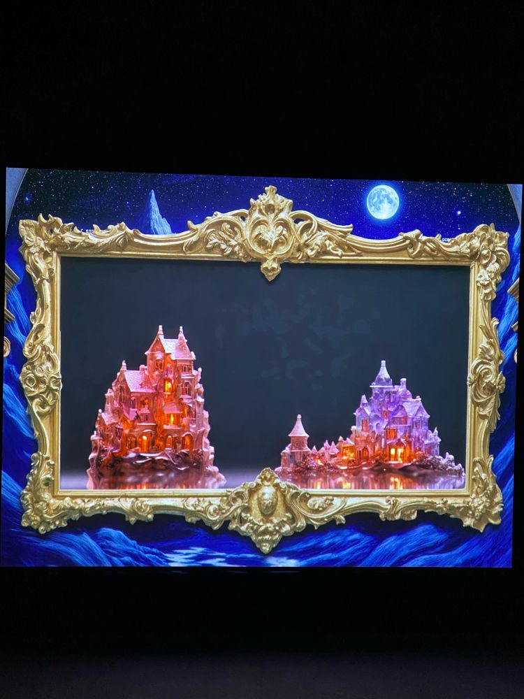 Ein digital dargestelltes Bild in einem goldenen, reich verzierten Rahmen. Innerhalb des Rahmens zwei detaillierte Miniaturgebäude mit vielen Türmen und Fenstern, die von innen orange-rot beleuchtet sind. Hintergrund ist dunkelblau mit einem Vollmond am Himmel und sternenähnlichen Punkten.