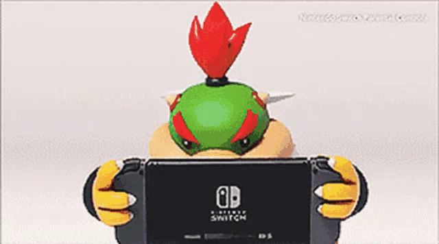 bowser is holding a nintendo switch in his hands and playing a video game .