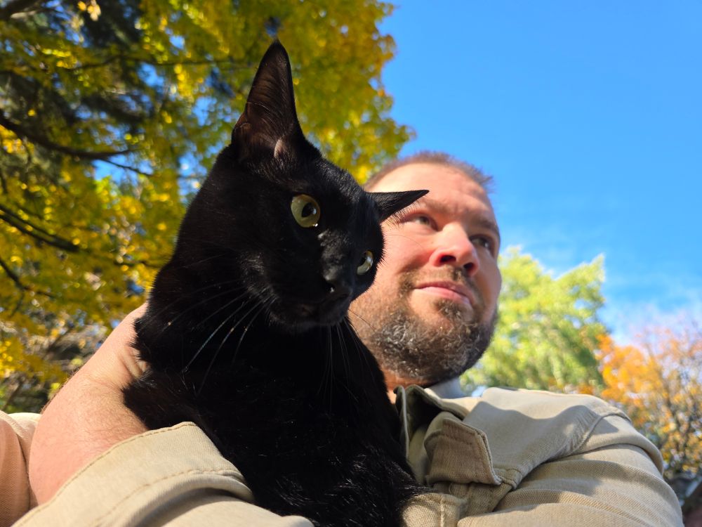 me holding my black cat outside on a sunny autumn day