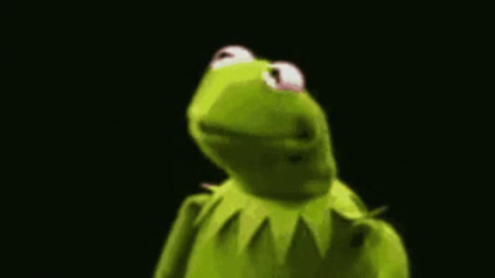 kermit the frog is standing in front of a black background and looking at the camera .