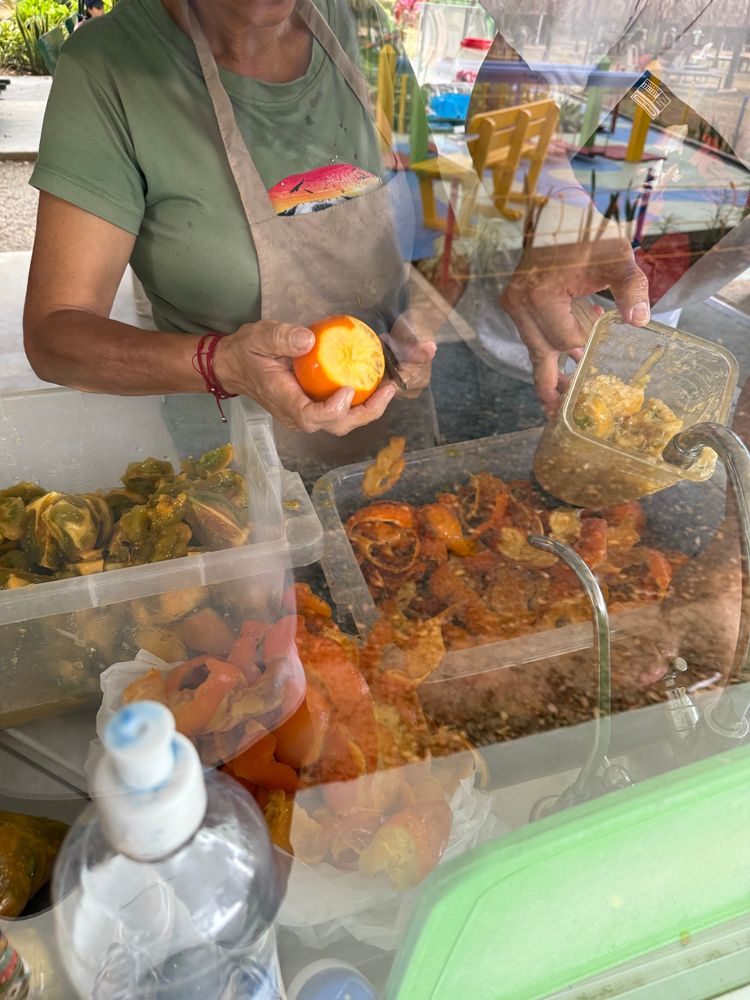 A market with a woman holding and peeling a ripe orange-colored lulo fruit. The inside of the fruit is greenish