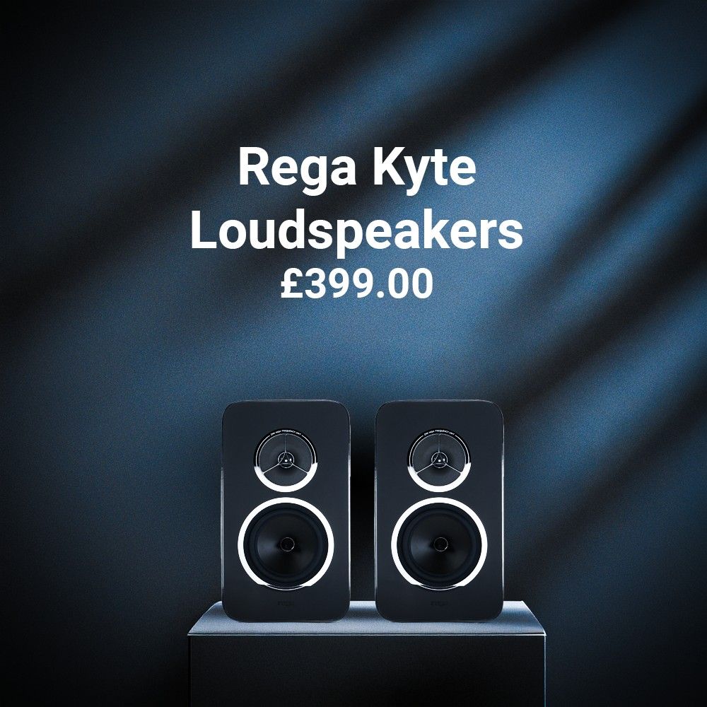 A pair of Rega bookshelf loudspeakers sit atop a cube-shaped podium. A navy blue background with plant-like shadows overcasting it forms as the backdrop for this image. White text in the middle of the image reads, "Rega Kyte Loudspeakers, £399.00"