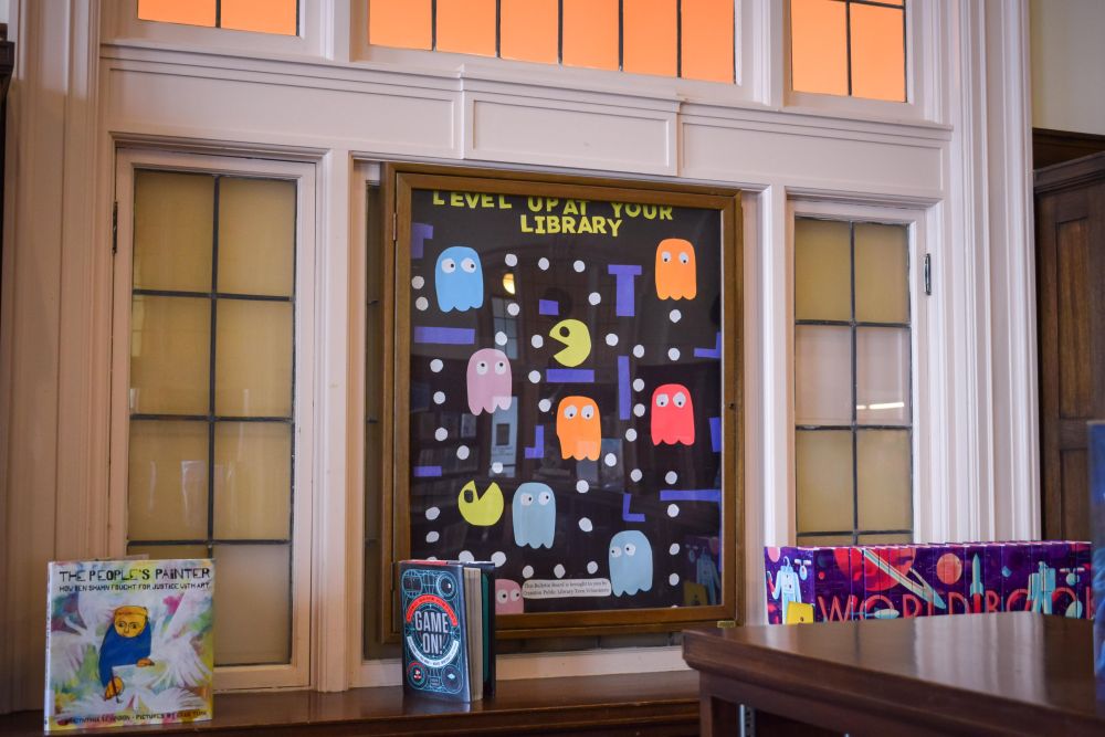 Window with construction paper art. Pac Man design with the words Level Up at your Library!