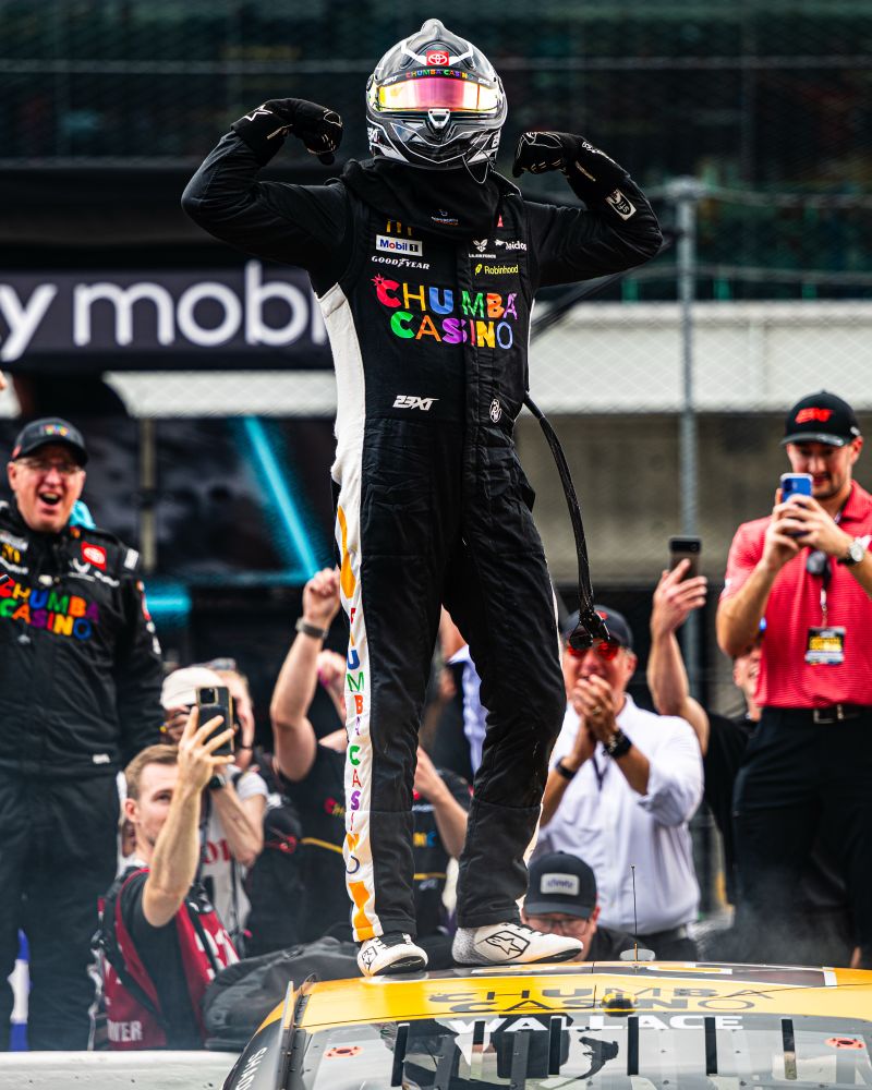 Bubba Wallace stands on his car and flexes after winning the Brickyard 400