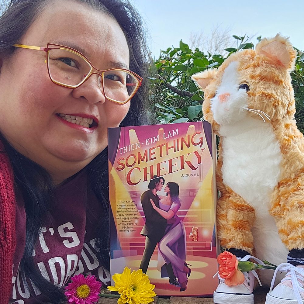Thien-Kim posing with her new romance novel Something Cheeky alongside a plushie version of Mr. Bobbins, who is featured in the book.