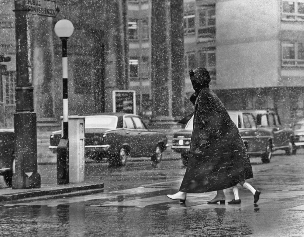 Frau im Regen mit Kind unter dem Mantel 