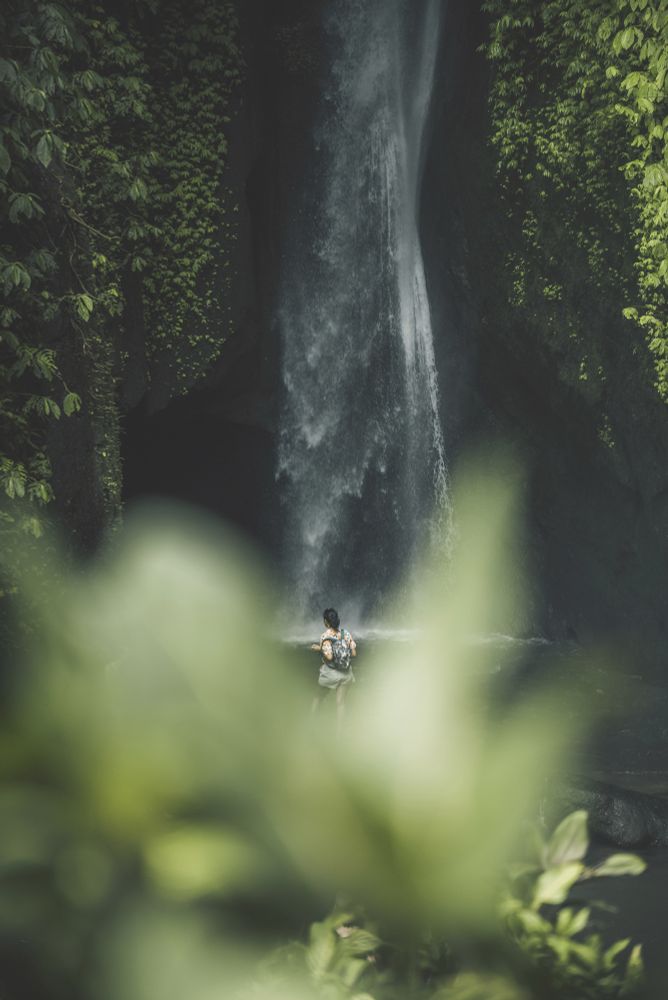 A woman taking off her backpack in front of a waterfall.