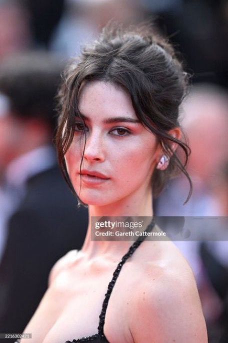 Gracie Abrams looking at the camera with her hair up in a bun and her bang pieces out  