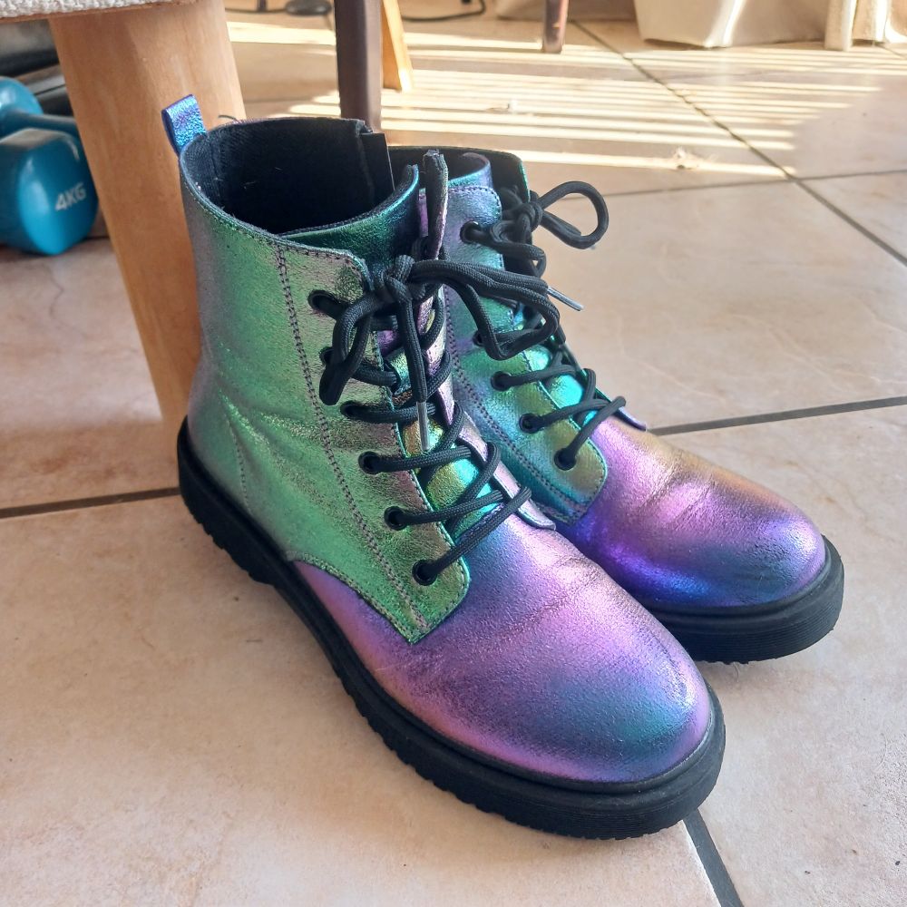A pair of iridescent boots on a tiled floor. The colours have shifted from purple/Indigo on the toe to green on the back.
