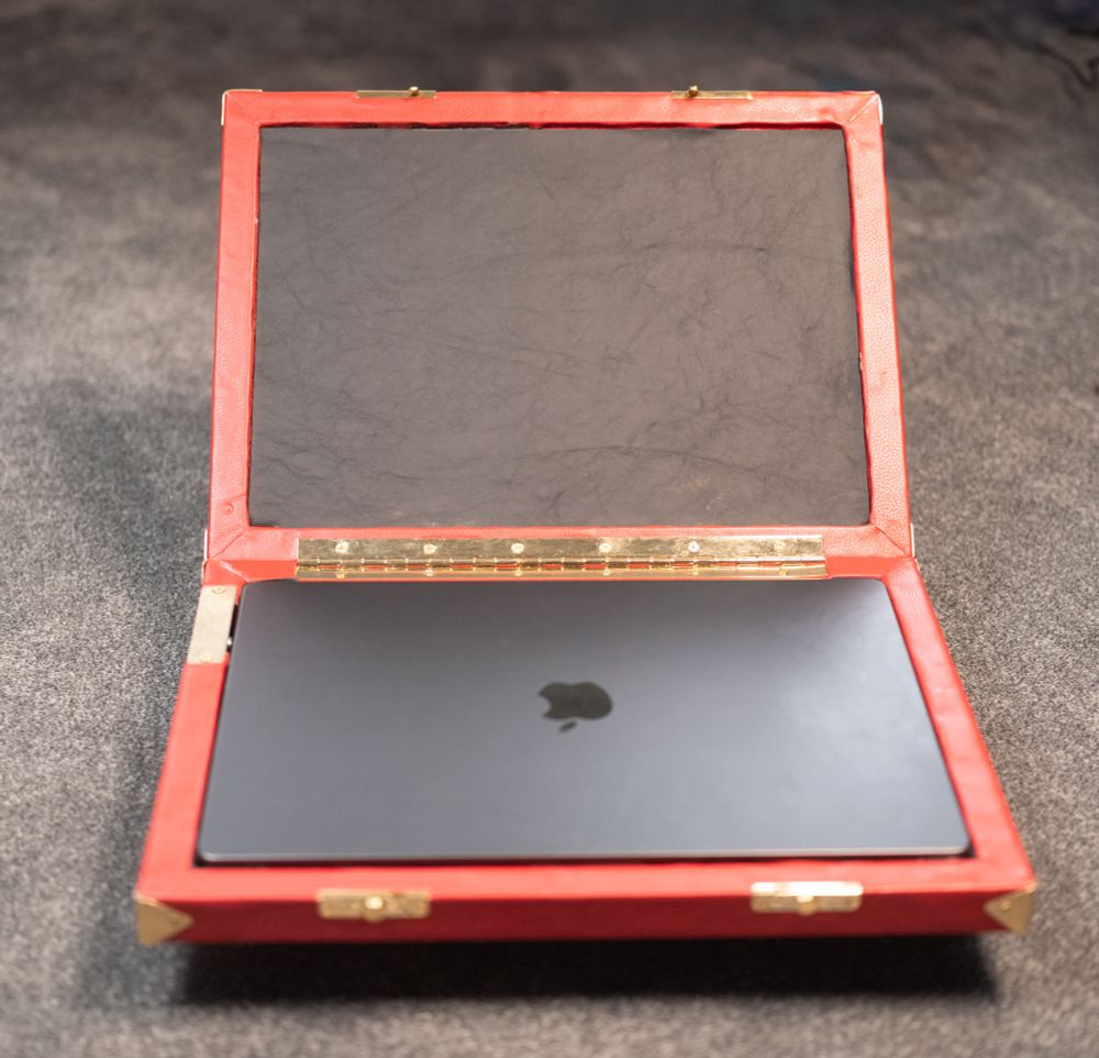 The same briefcase open to reveal a MacBook and black leather lining