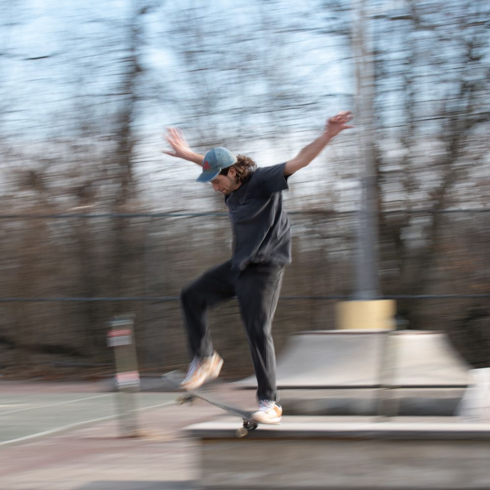 Man in a dark grey t-shirt dismounting off a grind. Similarly only his face and upper torso are sharp while the rest is blurred due to the motion