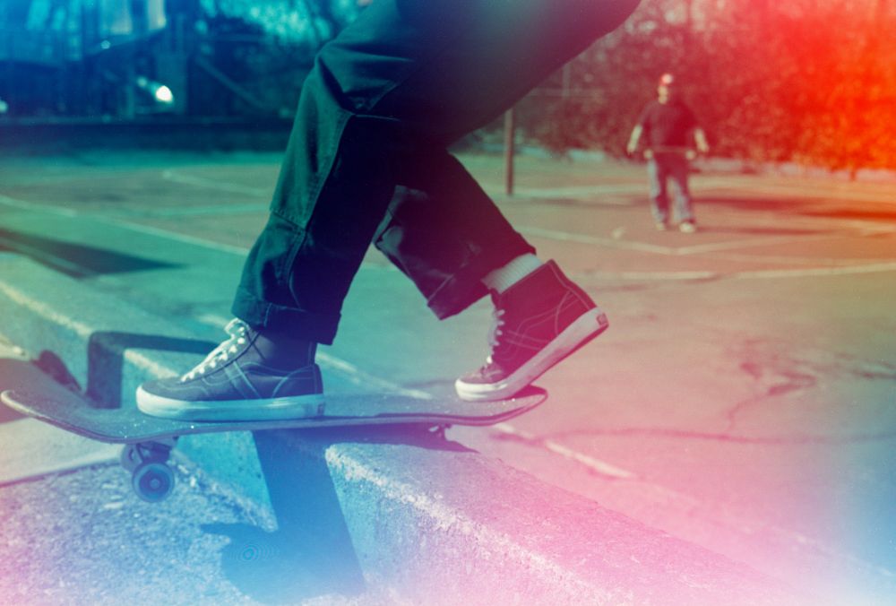 Close up photo of someone coming out of a front rock with another guy holding a skateboard in the background. The photo is a random hue because it was preexposed to colored light.