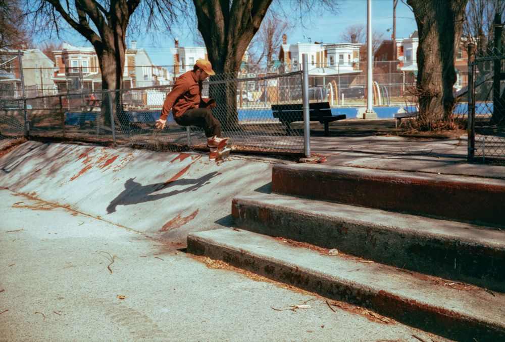 Photograph of a skateboarder coming off a set of 3 steps onto a relatively steep concrete bank at a sus angle